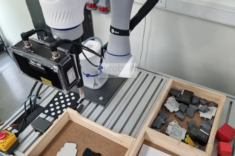 White cobot with a 3D camera above trays of small metal parts.