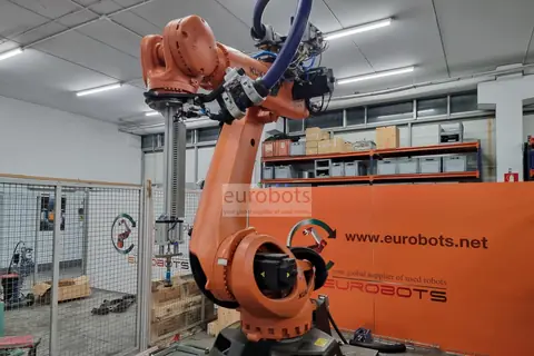 Orange KUKA robot with a pneumatic gripper inside a fenced test cell at Eurobots.