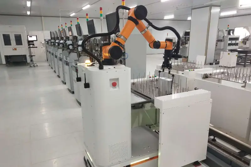 Orange collaborative arm on an autonomous mobile robot beside a row of production machines.
