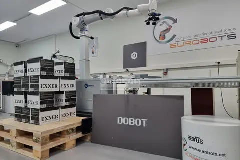 White collaborative robot on a lifting column next to a pallet of stacked boxes.